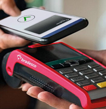 #Pracegover Um celular se aproximando da maquina de cartão para efetuar o pagamento