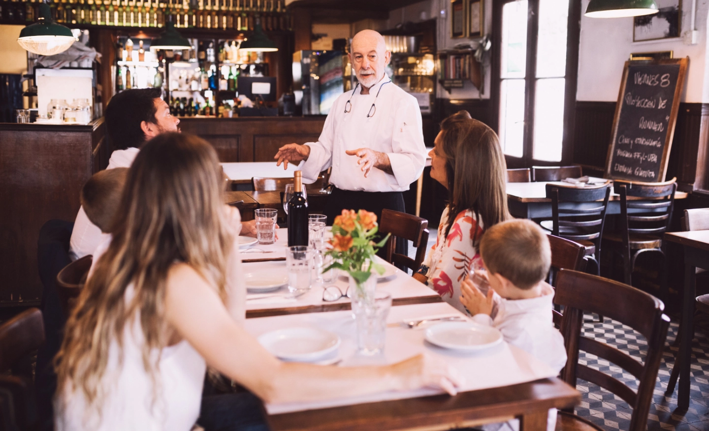 #BradescoAcessível #Pratodomundover Nas laterais, hágrafismos vermelhos. No centro, uma imagem de um chef de cozinha fazendo uma explicação para uma família sentada a mesa de um restaurante.