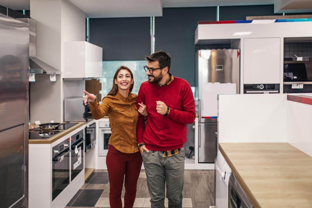casal em uma cozinha com mulher apontando para uma geladeira