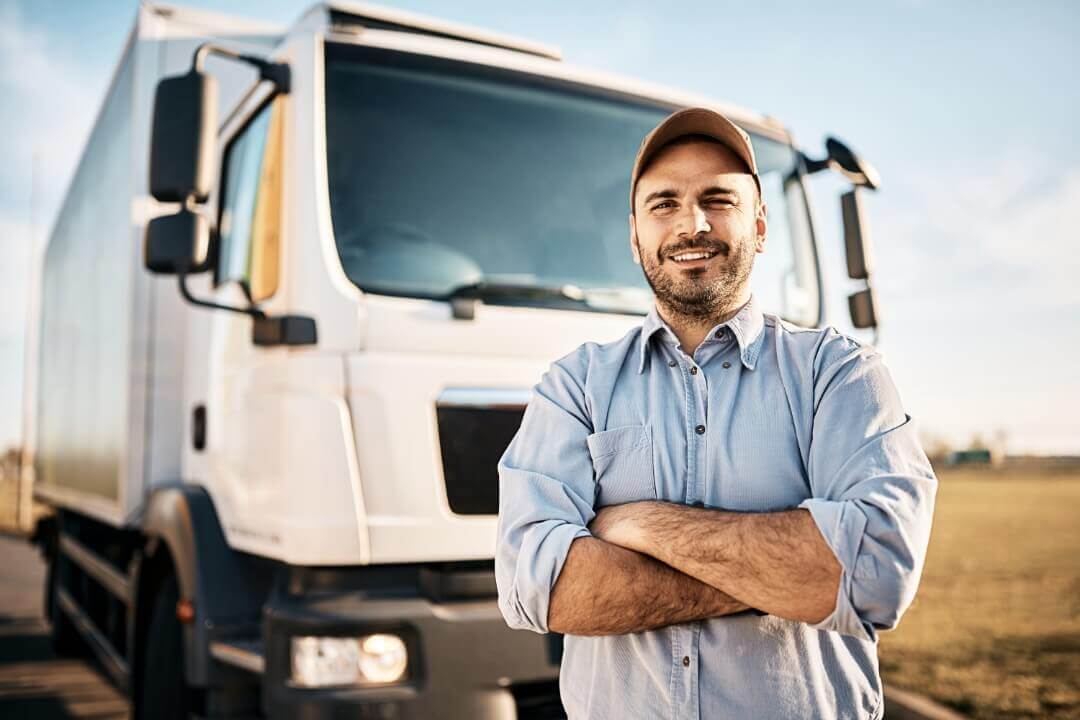 Homem sorrindo com os braços cruzados na frente de um caminhão